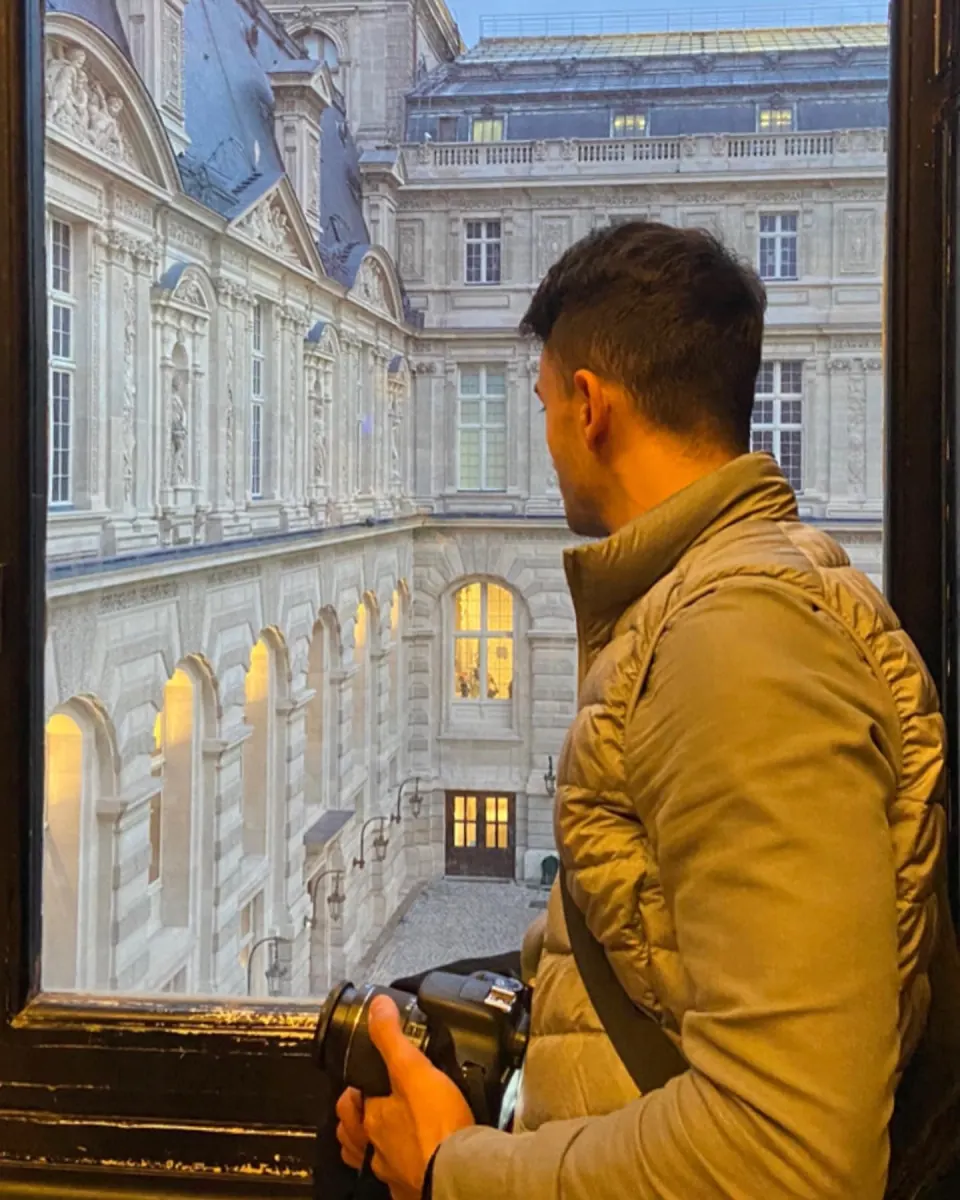Giovanni with a camera at a window above the Louvre courtyard, Paris