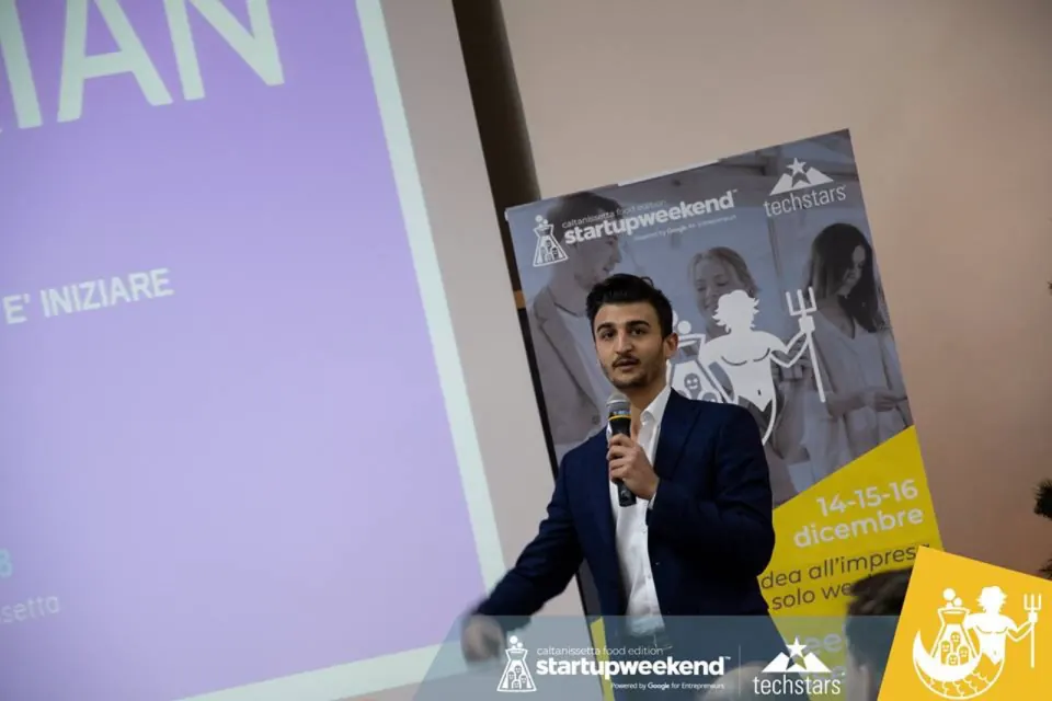 Giovanni on stage with a microphone at Startup Weekend by Techstars